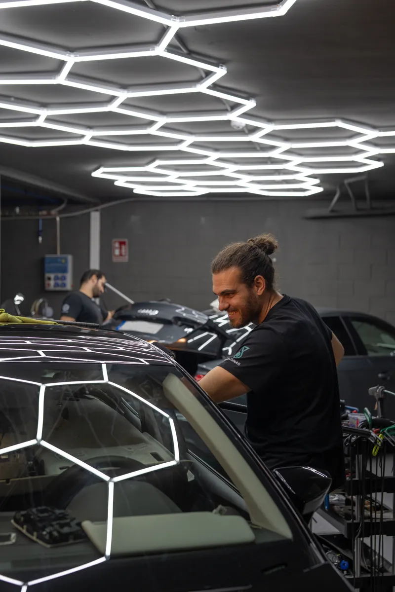 Técnico de DF Varilleros reparando una abolladura bajo las luces hexagonales, reflejadas en la carrocería